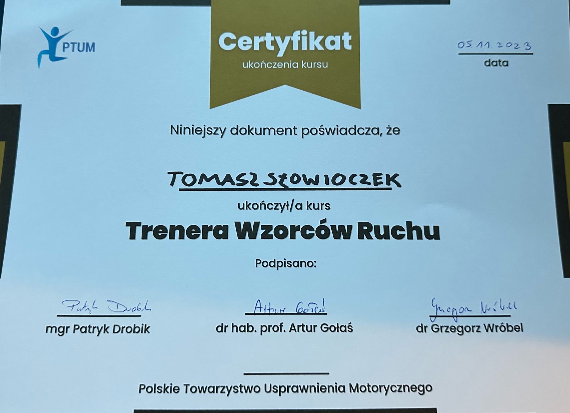 Zdjęcie dyplomu Trenera Wzorców Ruchu z Polskiego Towarzystwa Uprawnienia Motorycznego, z widocznym logo organizacji i podpisami certyfikujących ekspertów.